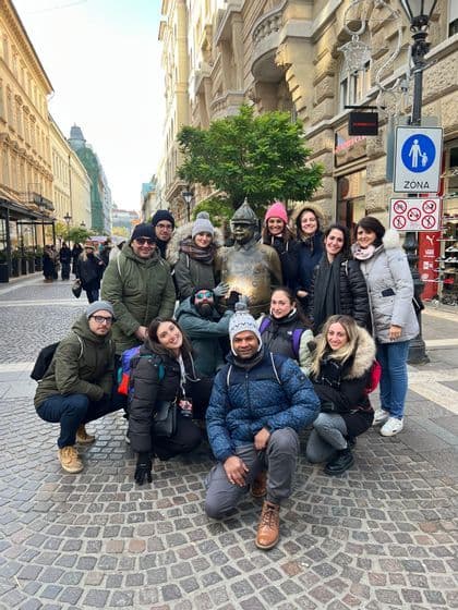 Un viaje en grupo de WeRoad con ropa de invierno posando para una foto grupal con una estatua de bronce en una calle adoquinada de la ciudad.
