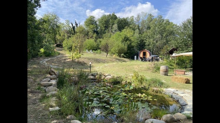 Un piccolo stagno con ninfee in un giardino verde con una capanna a forma di botte e un sentiero di pietra tortuoso che sale su per una collina.