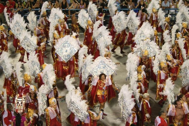 Vista aérea de muchos artistas con trajes de plumas rojos y blancos desfilando durante un carnaval.