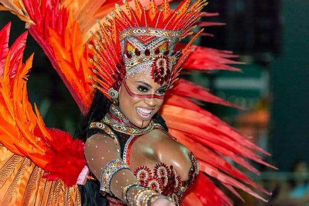 A woman smiles while dancing in an elaborate red and orange feathered carnival costume and headdress.