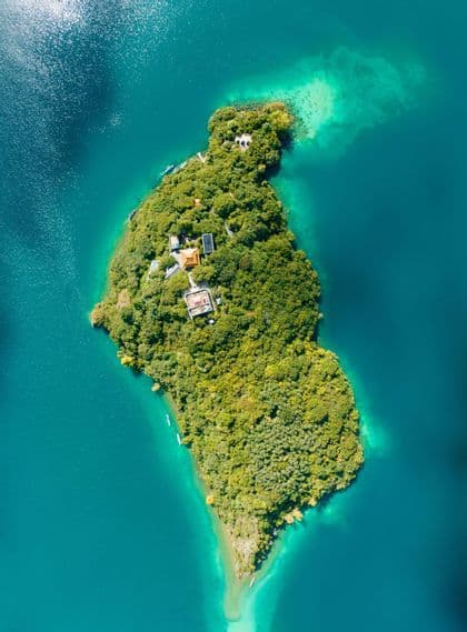 Una veduta aerea dall'alto di un'isola verde e lussureggiante con edifici immersi tra gli alberi, circondata da vivaci acque turchesi.