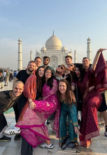 Un gruppo WeRoad in viaggio, con abiti tradizionali colorati, posa giocosamente davanti a un grande mausoleo di marmo bianco.