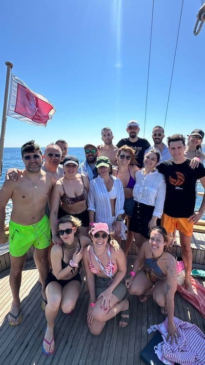 A WeRoad group trip poses together for a photo on the wooden deck of a boat, with the open sea behind them.