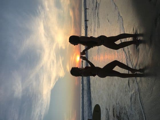 Due persone di un viaggio di gruppo WeRoad sono in silhouette su una spiaggia, che brindano al tramonto.