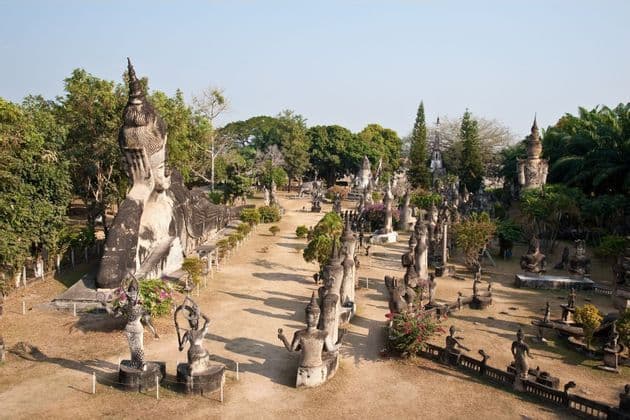 Ein Blick von oben auf einen Skulpturenpark mit einem riesigen liegenden Buddha und vielen weiteren zwischen Bäumen verteilten Statuen.