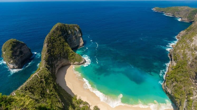 Eine Luftaufnahme einer grün bewachsenen Klippenformation, die in einen tiefblauen Ozean ragt und einen abgelegenen weißen Sandstrand mit türkisfarbenem Wasser bildet.