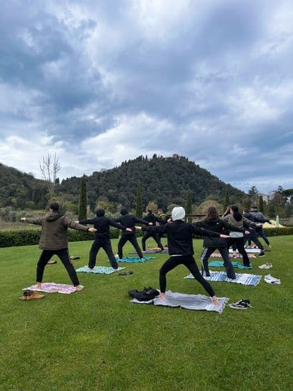 Un viaggio di gruppo WeRoad che pratica una posa yoga su un prato verde con una collina alberata sullo sfondo.