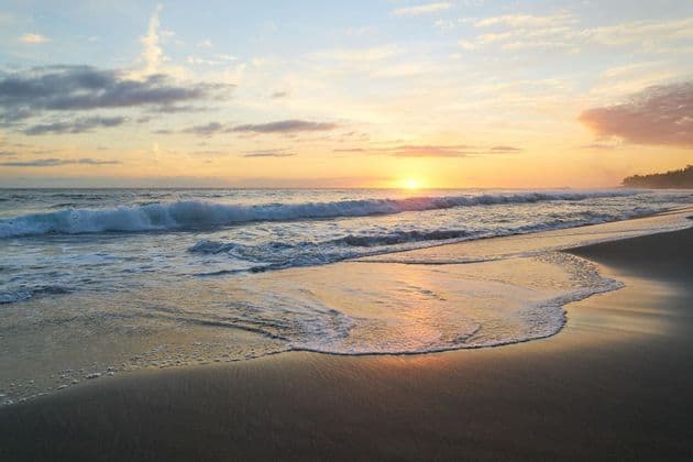 Die Sonne geht über dem Meer unter und taucht die Wellen, die am Sandstrand brechen, in ein goldenes Licht.