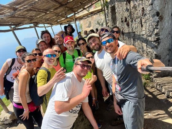 Un grupo de WeRoad se toma una selfie en un sendero soleado bajo un refugio rústico de madera.