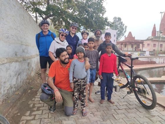 Un gruppo di ciclisti WeRoad in posa con bambini e adulti del luogo su un sentiero lastricato, con un tempio sullo sfondo.