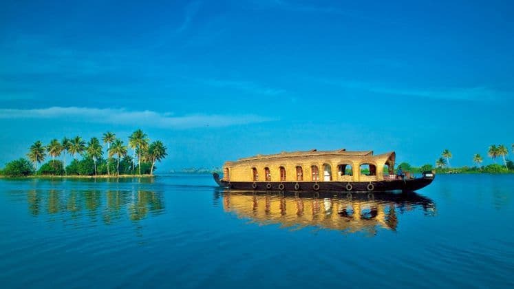 Ein traditionelles Holzhausboot mit Reetdach schwimmt auf ruhigem blauem Wasser, mit Palmen an einem fernen Ufer.