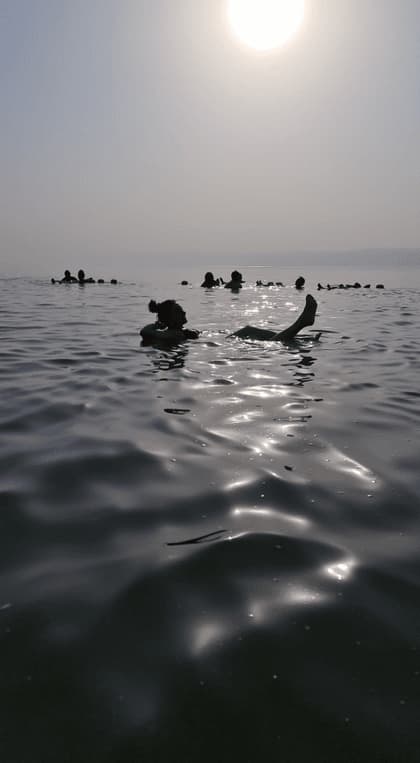 Sagome di un viaggio di gruppo WeRoad che galleggiano senza sforzo sulla schiena in acque calme sotto un sole luminoso e velato.