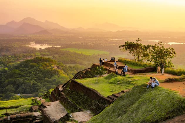 Un viaje en grupo de WeRoad se reúne en un mirador sobre ruinas antiguas, observando un atardecer sobre un valle exuberante con montañas distantes.