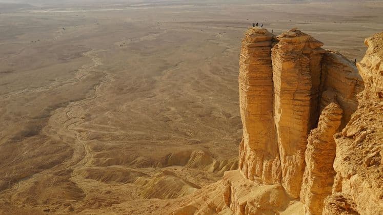 Un voyage de groupe WeRoad se tient au sommet d'une haute formation rocheuse surplombant un vaste paysage désertique aride.