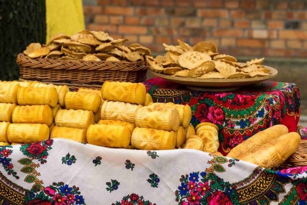 Variedad de quesos tradicionales con diseños y galletas saladas, exhibidos en una mesa con manteles florales coloridos.