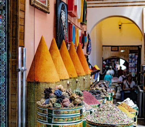 Colorful cone-shaped mounds of spices and bins of dried herbs are on display at a bustling market stall.