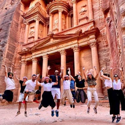 Un viaggio di gruppo WeRoad, con i partecipanti che saltano insieme per una foto davanti a un grande tempio antico scavato in una parete di roccia rossa.