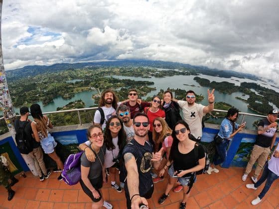 Un viaje en grupo de WeRoad se toma una selfie en un mirador con vistas panorámicas a lagos e islas verdes y montañosas.
