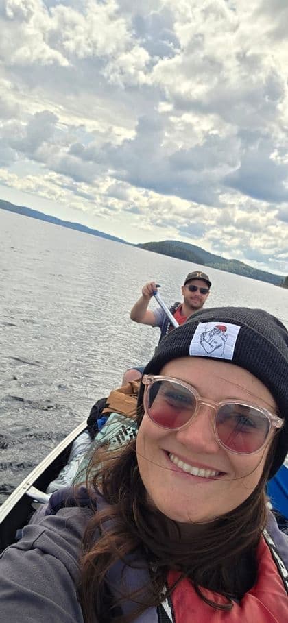 Eine WeRoad Gruppenreise mit einer Frau und einem Mann, die beim Paddeln in einem Kanu auf einem See mit Hügeln im Hintergrund ein Selfie machen.