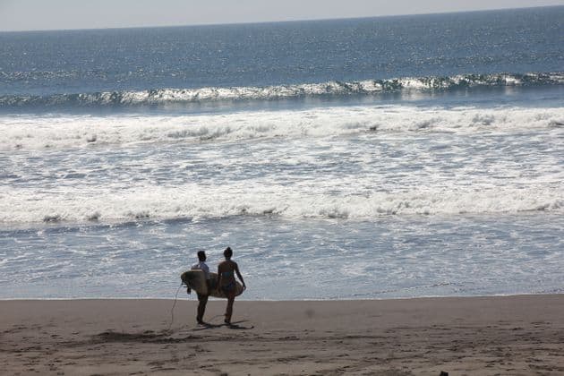 Un uomo e una donna trasportano tavole da surf camminando su una spiaggia sabbiosa verso le onde dell'oceano.