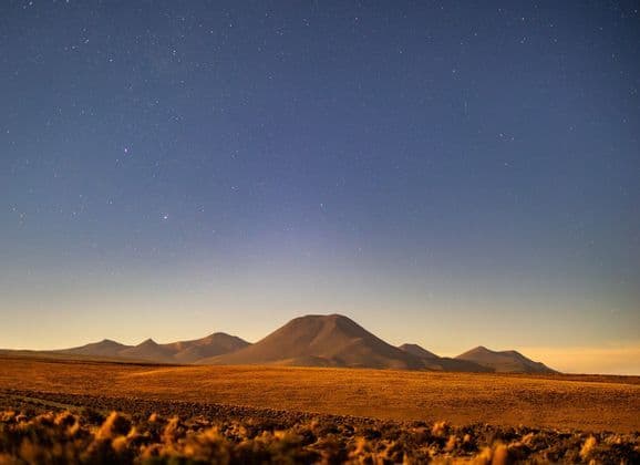 Una vasta pianura desertica con montagne ondulate in lontananza sotto un cielo notturno limpido e stellato.
