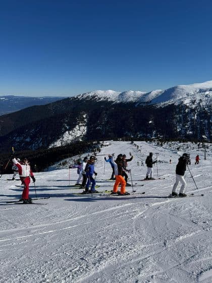 Eine WeRoad Gruppenreise posiert auf Skiern auf einem sonnigen, verschneiten Hang mit Bergen im Hintergrund unter einem klaren blauen Himmel.