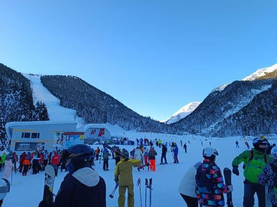 Un voyage de groupe WeRoad de skieurs dans une station de montagne enneigée, se préparant à monter les pistes sous un ciel bleu clair.