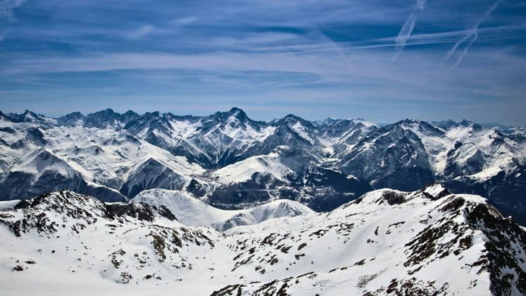Un'ampia vista di cime montuose innevate che si estendono fino all'orizzonte sotto un cielo azzurro.