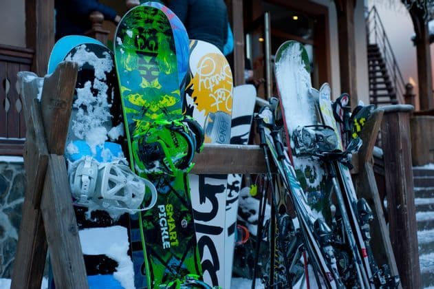 Una colección de coloridas tablas de snowboard y esquís cubiertos de nieve están apoyados en un estante de madera.