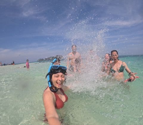 Eine WeRoad-Gruppenreise plantscht im klaren Meer, während eine Frau mit Schnorchelmaske ein lächelndes Selfie macht.