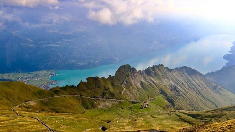 Vue aérienne d'une route sinueuse sur une crête de montagne verte, surplombant un grand lac turquoise dans une vallée.