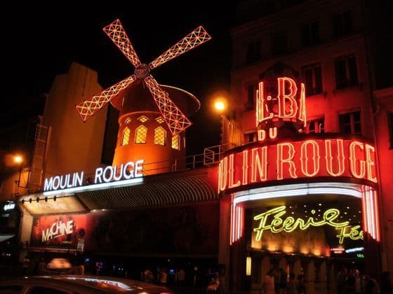 Le bâtiment du cabaret du Moulin Rouge la nuit, avec son iconique moulin rouge et son entrée illuminés par des néons rouges vifs.