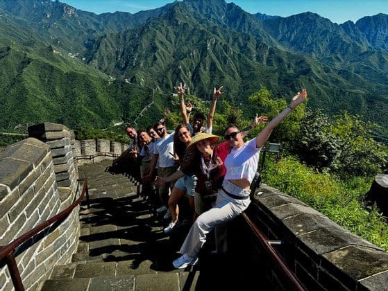Un voyage de groupe WeRoad posant sur les marches en pierre d'une grande muraille, avec des montagnes verdoyantes en arrière-plan.