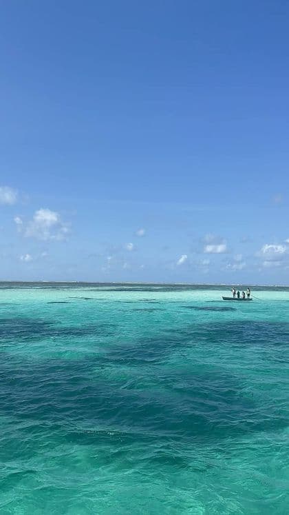 Un viaggio di gruppo WeRoad su una piccola barca che galleggia su un vasto oceano turchese, sotto un cielo azzurro limpido con nuvole leggere.