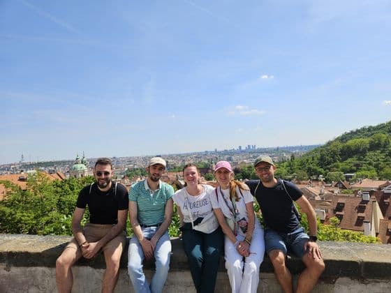 Un voyage de groupe WeRoad de cinq personnes assises sur un mur en pierre et souriantes, avec une vue panoramique sur la ville en arrière-plan.