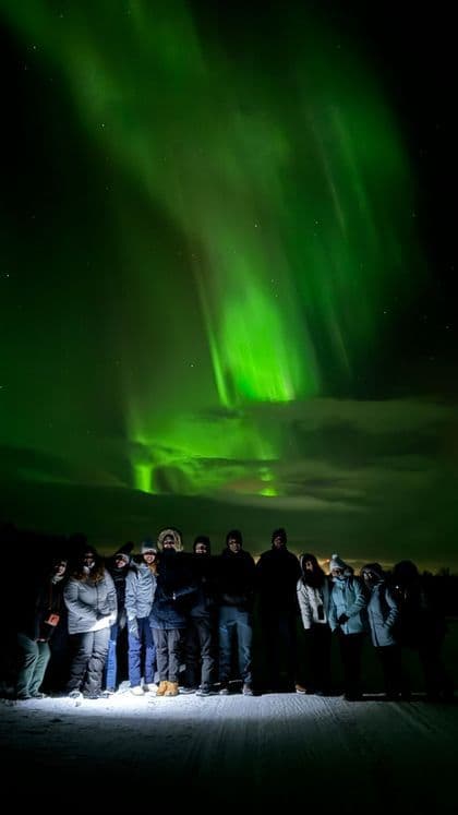 Un voyage de groupe WeRoad sur un paysage enneigé la nuit, posant pour une photo sous la lueur verte des aurores boréales.