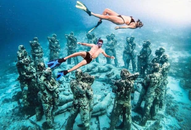 Two people from a WeRoad group trip snorkeling above a circular installation of submerged statues on the seabed.
