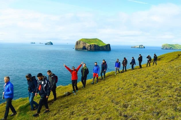 Eine WeRoad-Gruppe wandert in einer Reihe auf einem grasbewachsenen Hügel mit Meerblick und kleinen Inseln in der Ferne.