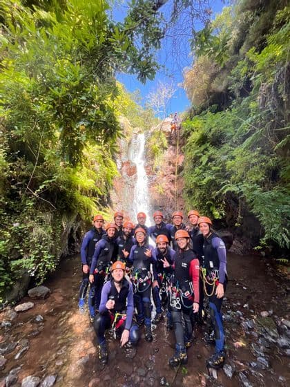 Un viaggio di gruppo WeRoad con mute e caschi posa per una foto in un ruscello alla base di una cascata durante un'attività di canyoning.