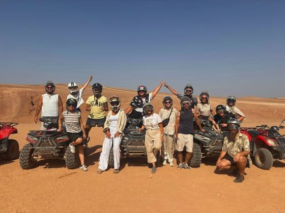 Un viaje en grupo de WeRoad con cascos posa para una foto con sus quads en un paisaje desértico soleado.