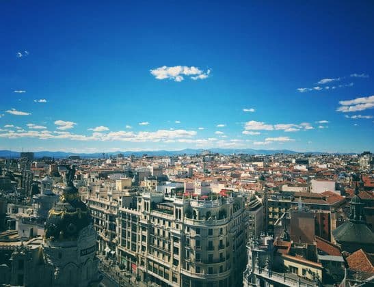 Una vista aerea di un paesaggio urbano denso con una cupola ornata, con montagne lontane all'orizzonte sotto un cielo azzurro chiaro.