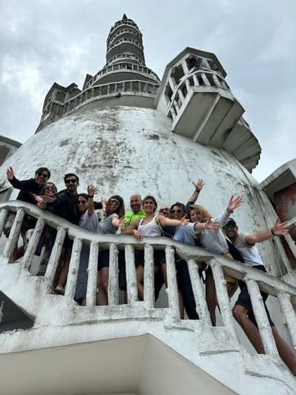 Un gruppo WeRoad in viaggio posa e saluta dalla scalinata di un ampio edificio bianco con cupola, sotto un cielo nuvoloso.