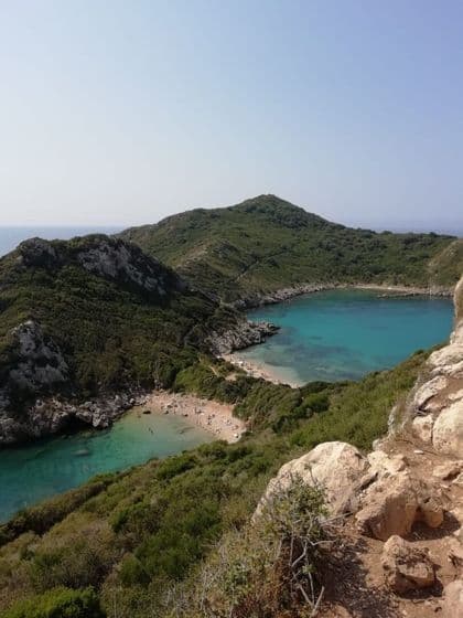 Vue aérienne de deux criques aux eaux turquoises et plages de sable, bordées de collines verdoyantes sous un ciel dégagé.