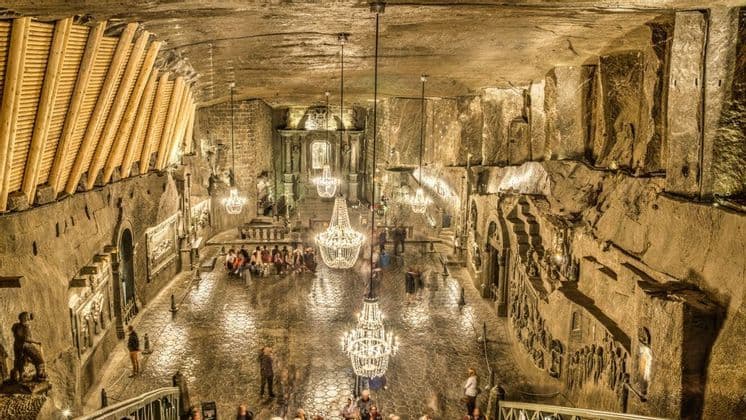 Un'immensa sala sotterranea, scavata nella roccia e illuminata da grandi lampadari di cristallo, con persone che camminano sul pavimento lucido.