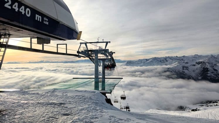 Eine WeRoad-Gruppenreise im Sessellift in einem verschneiten Skigebiet, aufsteigend über einem Wolkenmeer mit sichtbaren fernen Berggipfeln.