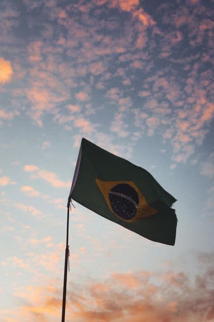 La bandera de Brasil en un mástil ondea contra un cielo con nubes rosadas dispersas al atardecer.