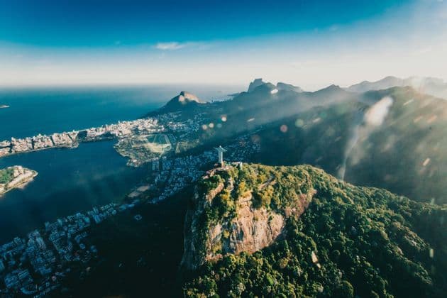 Una vista aerea del Cristo Redentore su una montagna rigogliosa che si affaccia su una città costiera, una laguna e l'oceano.