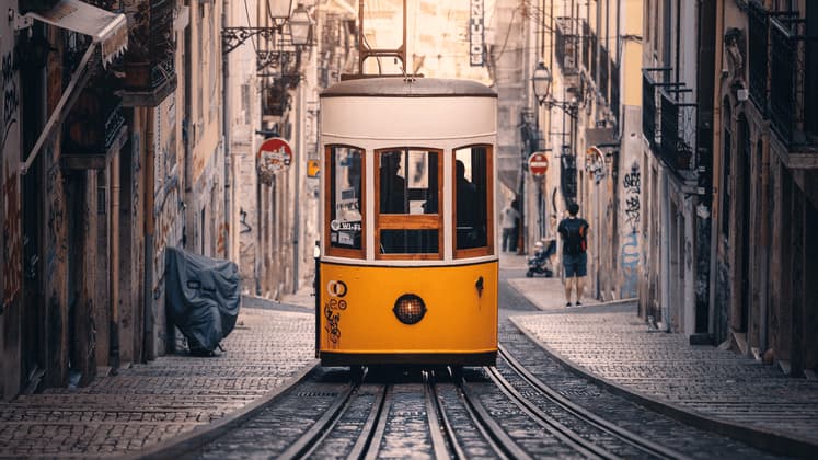 Un tram d'epoca giallo e bianco percorre una stretta via acciottolata costeggiata da edifici storici.