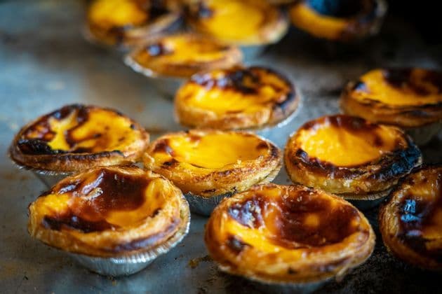 Primo piano di diverse crostatine portoghesi alla crema, o pastéis de nata, appena sfornate, con la superficie caramellata su un vassoio di metallo.