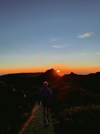 Eine WeRoad Gruppenreise wandert auf einem Steinpfad in den Bergen zum Sonnenaufgang.